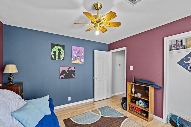 bedroom with a ceiling fan, visible vents, baseboards, and wood finished floors