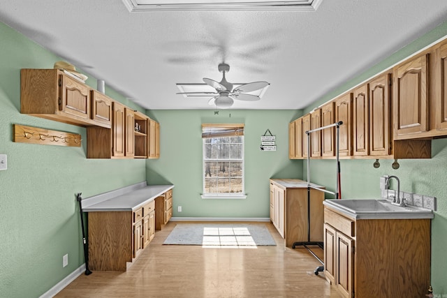 kitchen with a sink, light wood-style flooring, ceiling fan, and light countertops