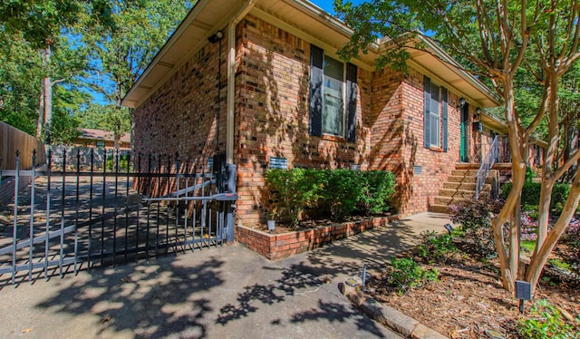 view of side of home featuring a gate, brick siding, and fence