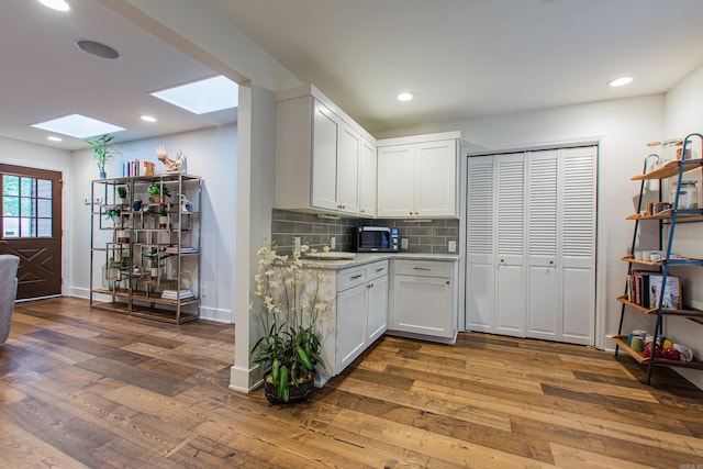 kitchen with a skylight, decorative backsplash, a sink, wood finished floors, and black microwave