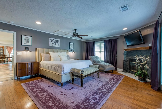 bedroom featuring a fireplace with flush hearth, visible vents, crown molding, and hardwood / wood-style flooring