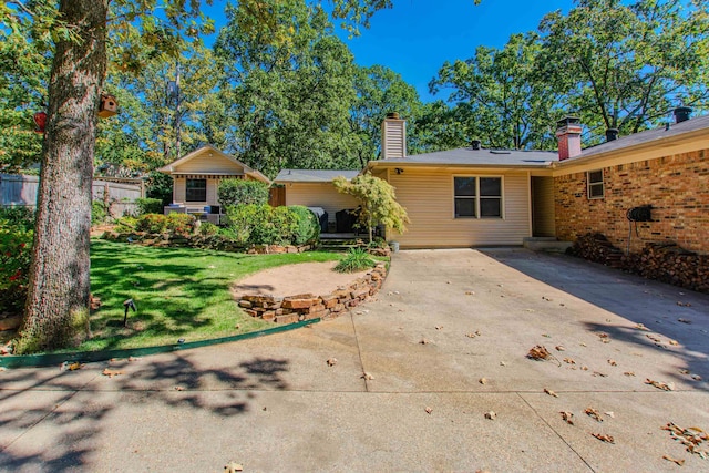 rear view of property with a chimney, concrete driveway, a lawn, a patio area, and fence