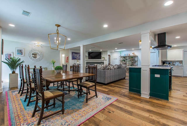 dining area with recessed lighting, a fireplace, wood finished floors, visible vents, and decorative columns