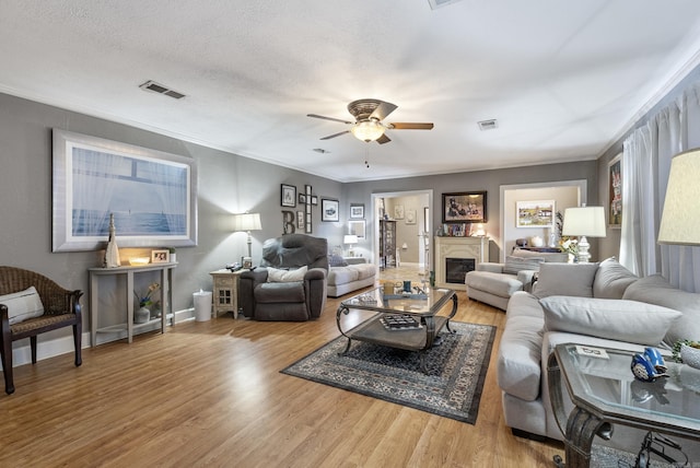 living room featuring a textured ceiling, a glass covered fireplace, wood finished floors, and visible vents