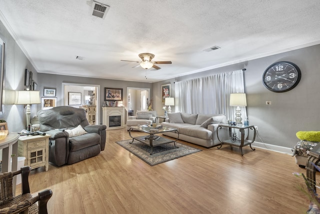 living room featuring light wood-type flooring, a glass covered fireplace, visible vents, and ornamental molding