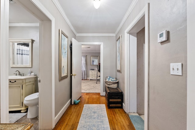 hall featuring light wood-type flooring, baseboards, ornamental molding, and a sink