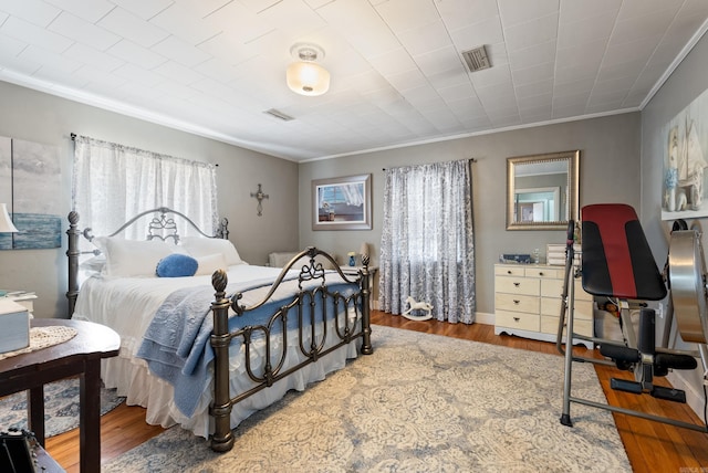 bedroom with visible vents, crown molding, and wood finished floors