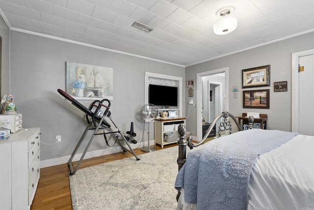 bedroom with ornamental molding, visible vents, baseboards, and wood finished floors