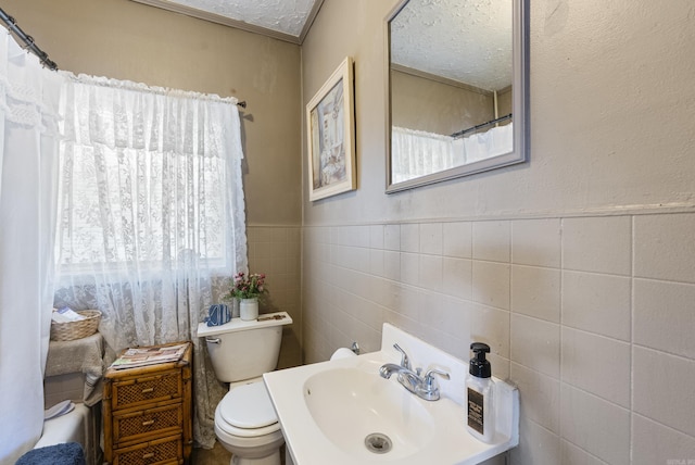 bathroom featuring a shower with shower curtain, toilet, a wainscoted wall, a sink, and tile walls