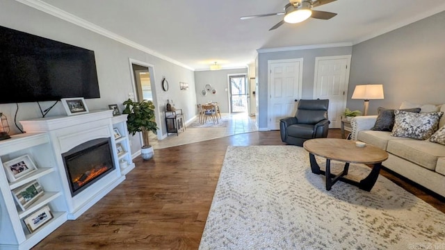 living area with dark wood-style floors, baseboards, crown molding, and a glass covered fireplace