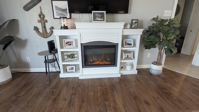 living area featuring wood finished floors, a glass covered fireplace, and baseboards