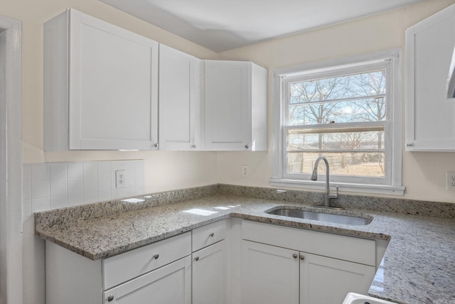 kitchen featuring light stone counters, white cabinets, and a sink