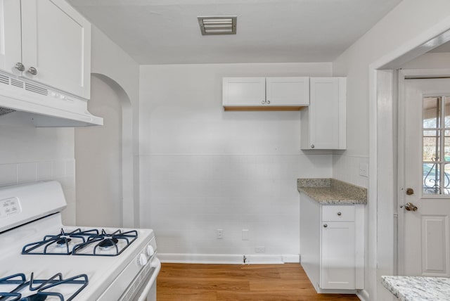 kitchen with white gas range oven, visible vents, light wood-style flooring, under cabinet range hood, and white cabinetry