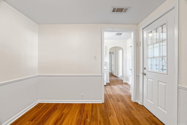 hallway with arched walkways, a wainscoted wall, wood finished floors, and visible vents