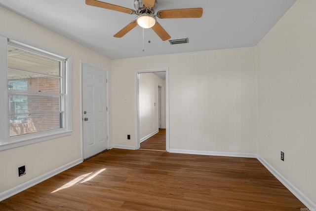 empty room with a ceiling fan, baseboards, visible vents, and wood finished floors