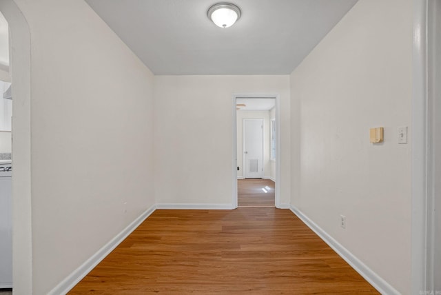 hallway featuring arched walkways, light wood-style flooring, and baseboards