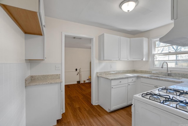 kitchen featuring white gas range oven, wood finished floors, under cabinet range hood, white cabinetry, and a sink