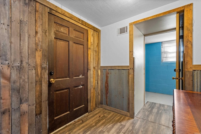 entryway with concrete block wall, visible vents, wainscoting, wood finished floors, and a textured ceiling