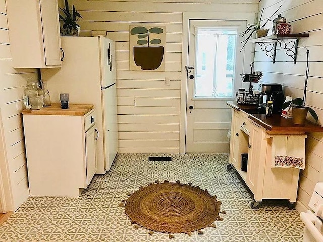 kitchen with light floors, freestanding refrigerator, and wooden walls