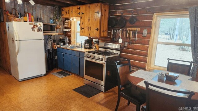 kitchen with appliances with stainless steel finishes, a sink, log walls, and light floors