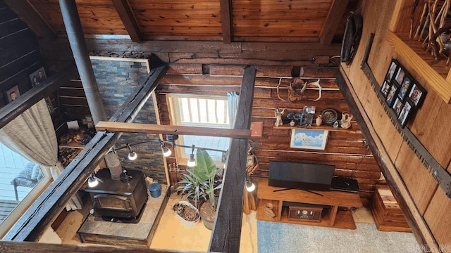 living area featuring rustic walls, beam ceiling, wooden ceiling, and a wood stove