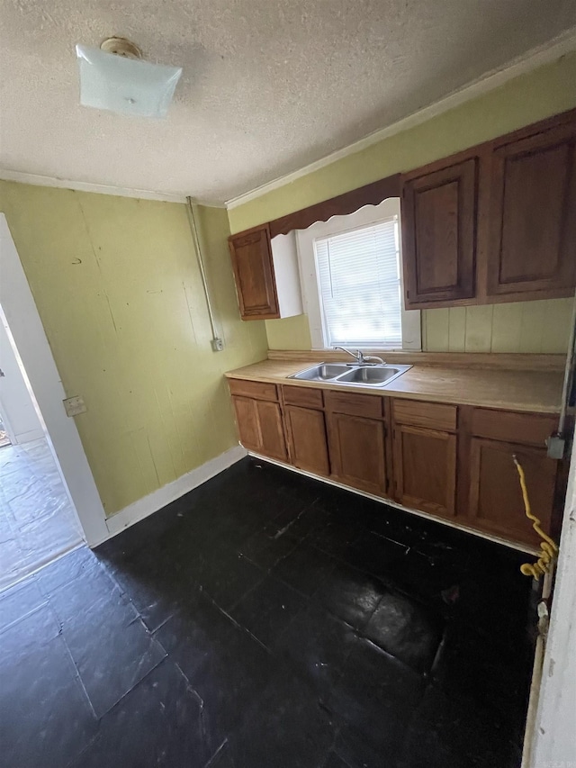 kitchen featuring baseboards, a sink, light countertops, a textured ceiling, and brown cabinets