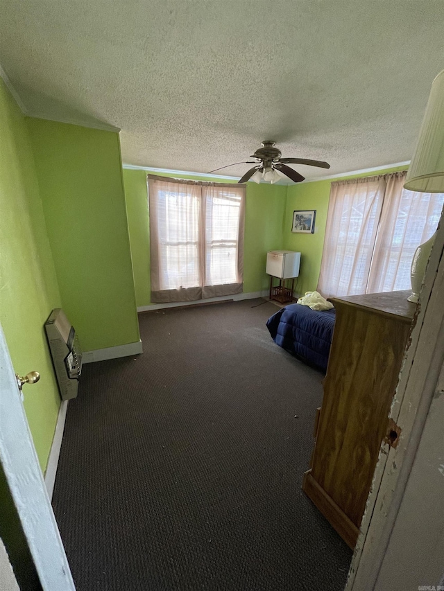 unfurnished bedroom featuring heating unit, a textured ceiling, carpet floors, baseboards, and ceiling fan