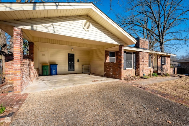 view of front of house featuring a chimney, an attached carport, concrete driveway, and brick siding