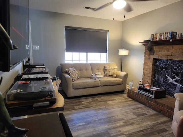 living room with a fireplace, visible vents, a ceiling fan, a textured ceiling, and wood finished floors