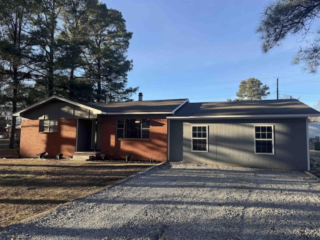 ranch-style house featuring gravel driveway and brick siding