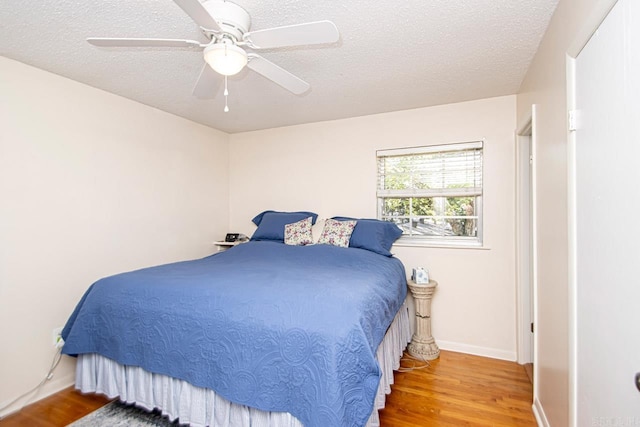 bedroom featuring ceiling fan, a textured ceiling, baseboards, and wood finished floors