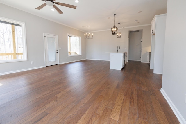 unfurnished living room featuring crown molding, dark wood-type flooring, a sink, baseboards, and ceiling fan with notable chandelier