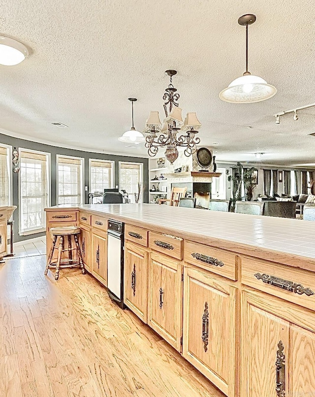 kitchen with light brown cabinetry, a fireplace, light wood-style flooring, and decorative light fixtures