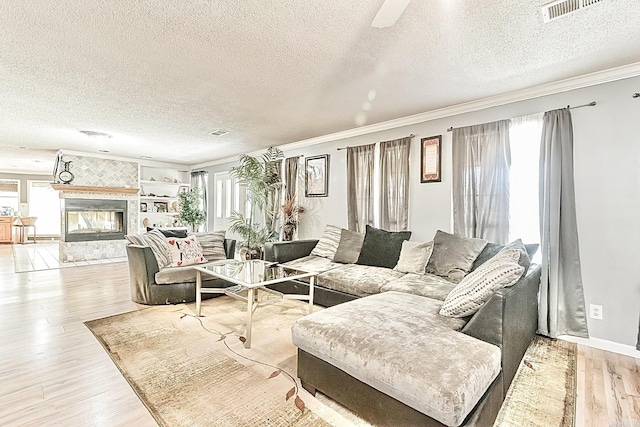 living area with a wealth of natural light, visible vents, a tiled fireplace, and wood finished floors