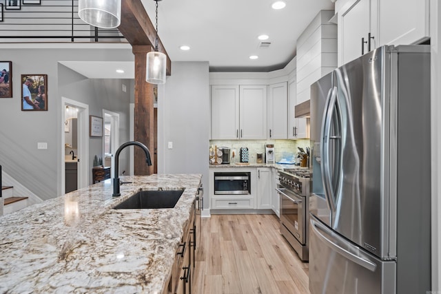 kitchen with light wood finished floors, stainless steel appliances, backsplash, white cabinets, and a sink