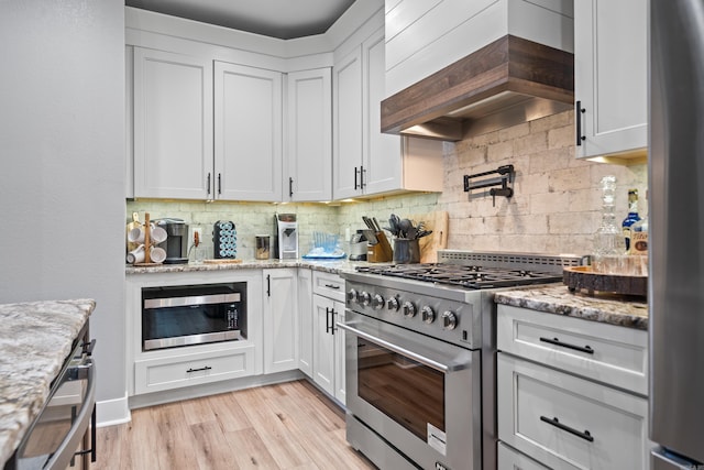 kitchen featuring appliances with stainless steel finishes, light stone countertops, custom range hood, and white cabinetry