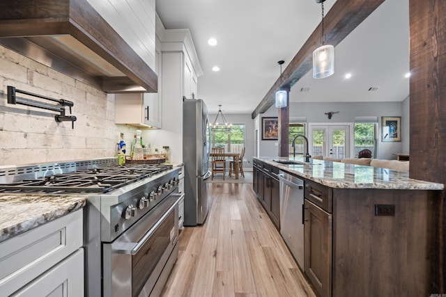 kitchen featuring dark brown cabinetry, stainless steel appliances, wall chimney range hood, white cabinetry, and a sink