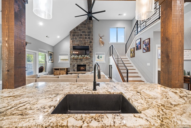 kitchen with ceiling fan, light stone countertops, a fireplace, high vaulted ceiling, and a sink