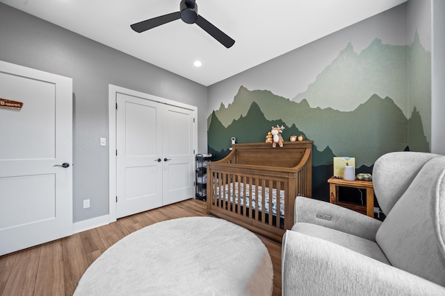 bedroom with baseboards, ceiling fan, wood finished floors, a nursery area, and a closet