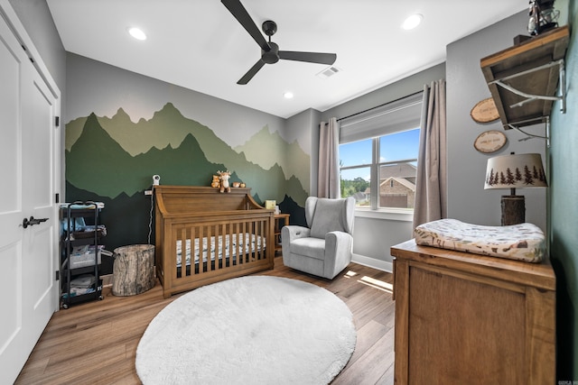 bedroom featuring a nursery area, wood finished floors, visible vents, and recessed lighting