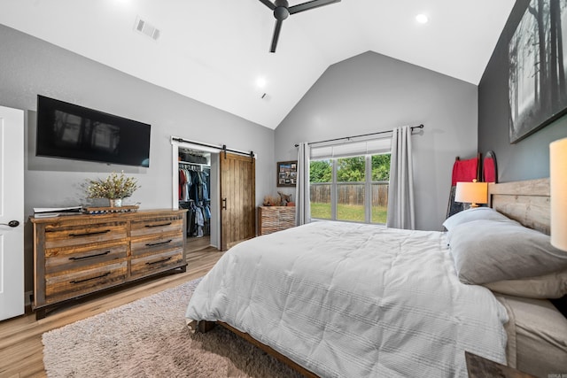 bedroom with a walk in closet, visible vents, a barn door, wood finished floors, and high vaulted ceiling