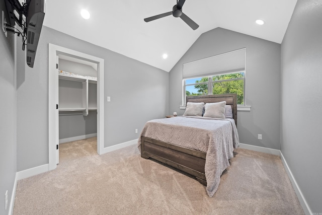 bedroom featuring light carpet, baseboards, lofted ceiling, ceiling fan, and a walk in closet