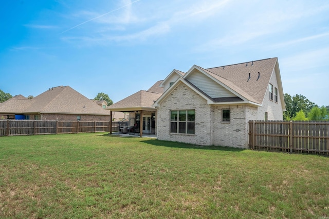 rear view of property with a fenced backyard, brick siding, roof with shingles, a lawn, and a patio area