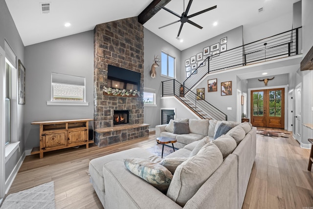 living room with visible vents, stairway, wood finished floors, a stone fireplace, and a healthy amount of sunlight