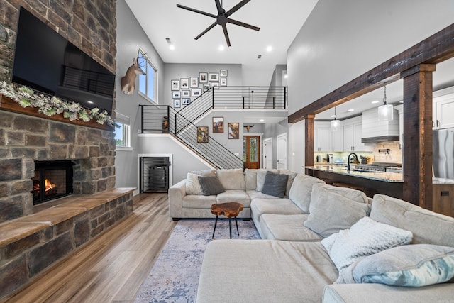 living room featuring a high ceiling, a ceiling fan, a stone fireplace, wood finished floors, and stairs