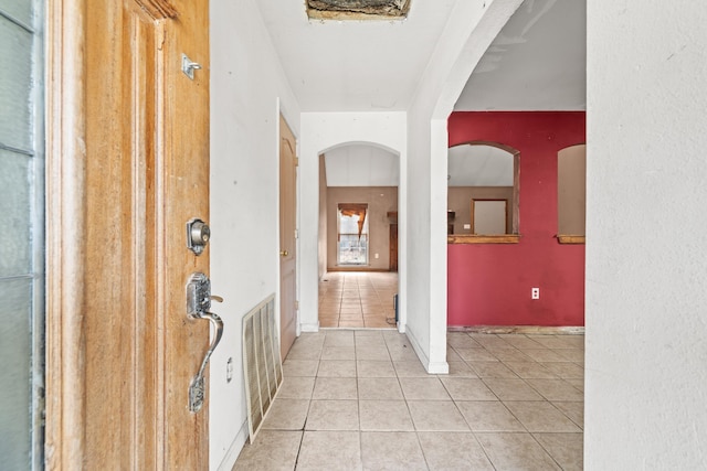 corridor with light tile patterned floors, visible vents, arched walkways, and baseboards