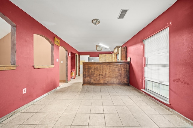 empty room featuring arched walkways, a dry bar, light tile patterned floors, visible vents, and a textured wall