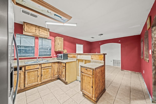 kitchen with stainless steel fridge, visible vents, arched walkways, a peninsula, and a sink