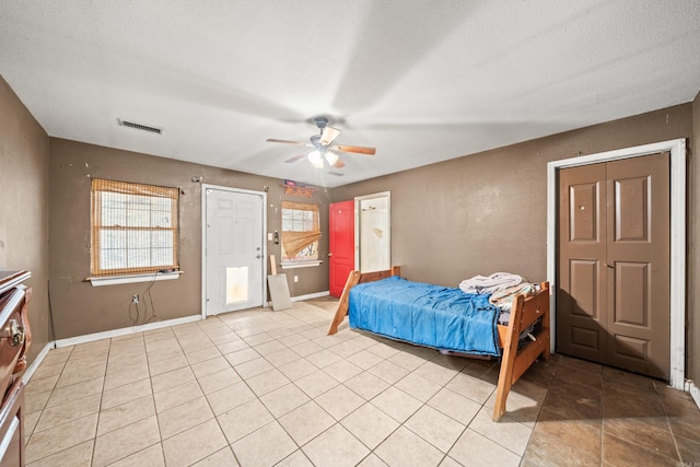 bedroom with light tile patterned floors, visible vents, a ceiling fan, a textured ceiling, and baseboards