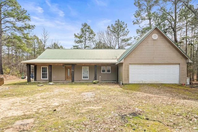 view of front of house with a garage, covered porch, dirt driveway, and metal roof